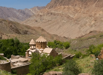 Aerial view of the UNESCO World Heritage Site St. Stepanos Monastery, nestled in lush green hills, with its stone buildings and church bathed in bright sunlight under a clear blue sky