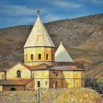 View of St. Thaddeus Church, a UNESCO World Heritage Site, showcasing its striking black and white stone architecture and domed roof set against a rugged mountain backdrop