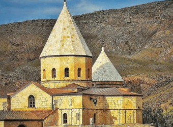 View of St. Thaddeus Church, a UNESCO World Heritage Site, showcasing its striking black and white stone architecture and domed roof set against a rugged mountain backdrop