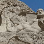 Ancient rock relief of Hercules at the Bisotun UNESCO World Heritage Site in Kermanshah, Iran, showing the Greek hero reclining on a stone platform beneath the cliffs